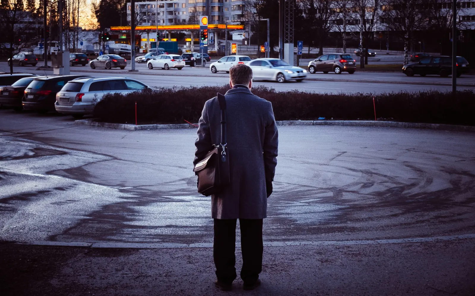 A man with a briefcase standing still in a parking lot at dusk